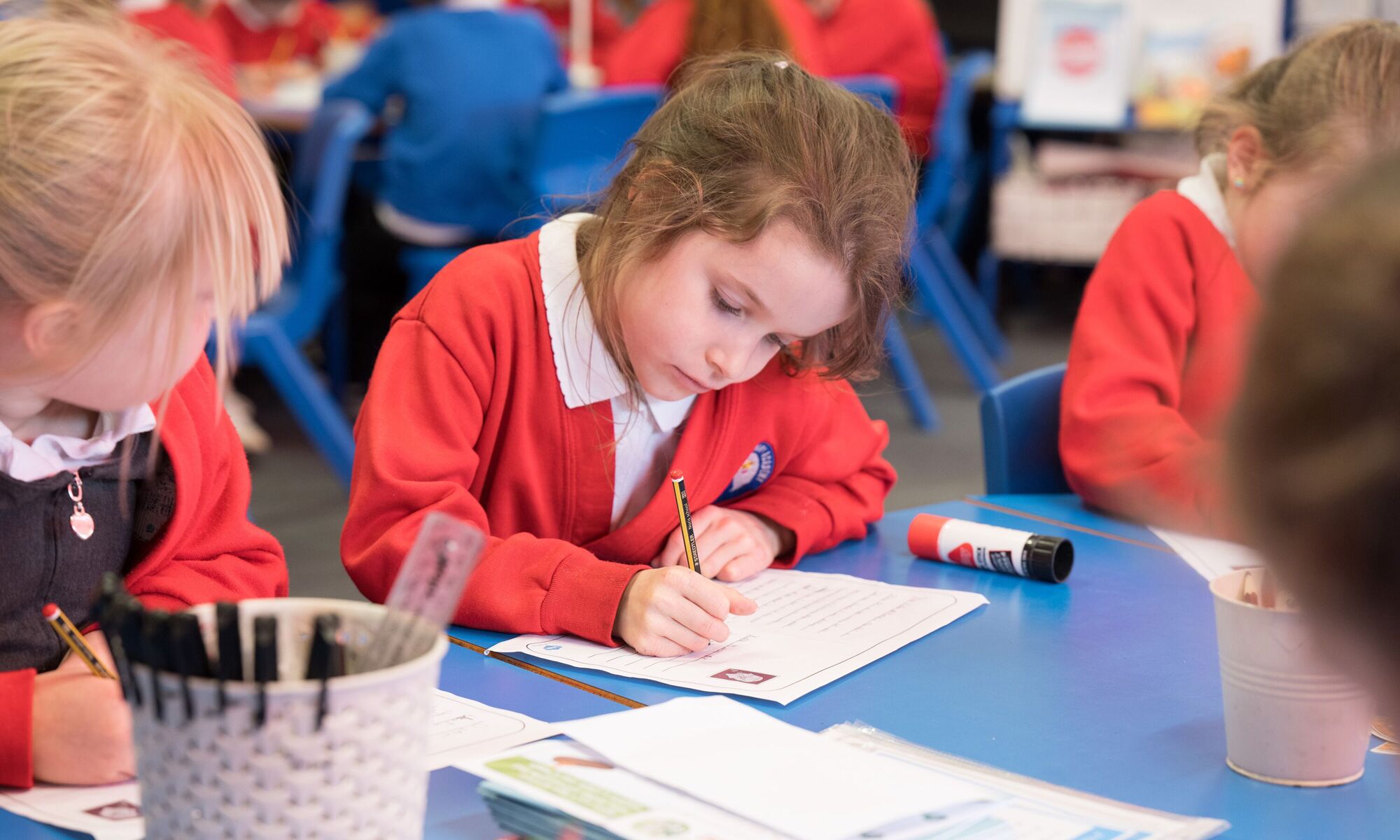 Starbeck Primary Academy - pupil writing in notepad in red school uniform